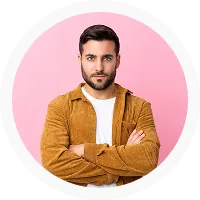 Man with dark hair and beard wearing a brown jacket and white shirt, standing with arms crossed.
