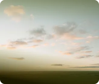 Soft pastel sky with scattered clouds above a dark, blurry horizon at dusk.